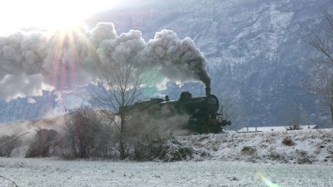Historic steam train rolling through the snowy valley in a winter day