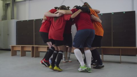 Zoom in shot of female team of professional soccer players huddling and running in place while getting ready for match in locker room