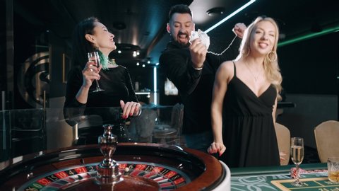 Excited group of bearded man and two beauty woman are winning at casino roulette table