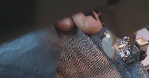 Close-Up Man's Hand Sewing With Denim Jeans On A Sewing Machine. Alteration Jeans, Hemming A Pair Of Jeans, Handmade Garment Industrial Concept. Cinema 4k Video. C4K