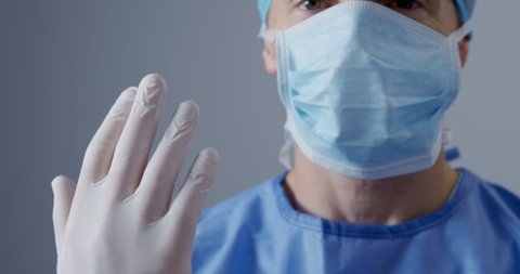 Front view close up of a Caucasian male surgeon at work in a hospital operating theatre wearing scrubs, a surgical cap and mask. Healthcare workers in the Coronavirus Covid19 pandemic
