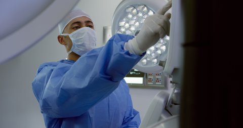 Mixed race male healthcare professional wearing a surgical cap, mask, gown and gloves, at work in a hospital operating theatre. Healthcare workers in the Coronavirus Covid19 pandemic