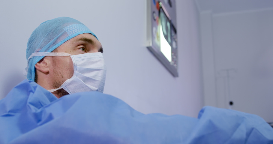 Side view close up of a Caucasian male healthcare professional wearing a surgical cap, mask. Healthcare workers in the Coronavirus Covid19 pandemic Royalty-Free Stock Footage #1043121766