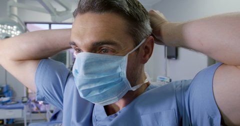Front view close up of a Caucasian surgeon male healthcare worker in a hospital putting on a surgical mask, slow motion. Healthcare workers in the Coronavirus Covid19 pandemic