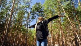 4k video of beautiful smiling woman hiking in the forest and stretching hands to the sun, trees and blue sky