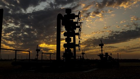 Silhouette of well head manifold in the oilfield at a cloudy sunset. Timelapse