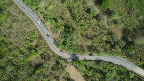 Aerial view of curvy rural road with cars speeding. Tropical forest landscape. 4K drone video.	