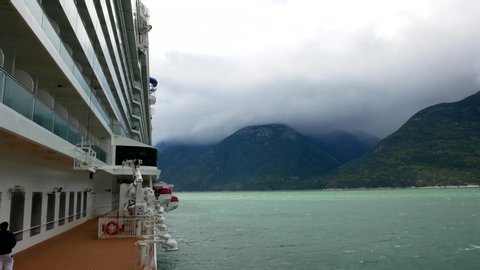 Skagway, Alaska - Sept, 15 2019: Timelapse view of clouds and cruise ship lifeboats and crew members working on open deck taken from inside a luxury cruise ship during cold day in Alaska.