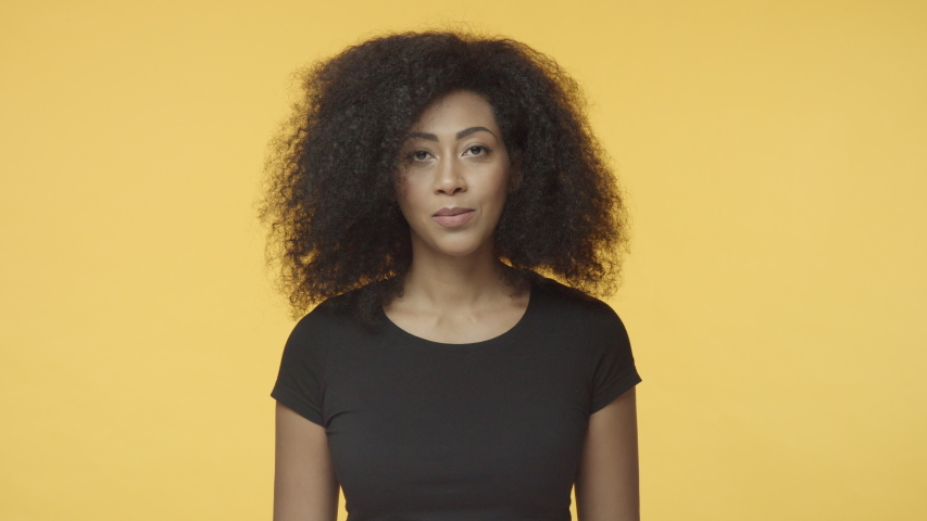 Girl confirm rumors with pleased smile. African-american female with afro hairstyle in black t-shirt, nod in agreement, give positive reply with satisfied smile, talking, agree, yellow background | Shutterstock HD Video #1043149756