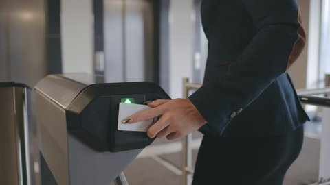 Businesswoman pass the electronic turnstile with plastic card entering modern office business center. Lady in formal clothes use card to access control
