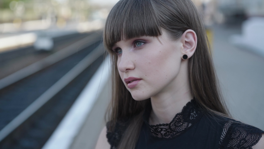 Close portrait of attractive girl looks around on railway station and smiles gently. 4K