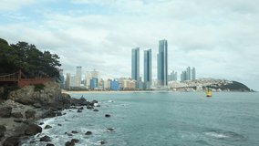 Scenic slow motion video of awesome rocky beach, sea and skyscrapers in Busan in South Korea. Beautiful summer cloudy look  in resort city of Republic of Korea