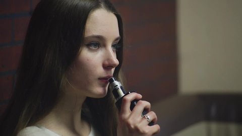 Vaping teenager with problem skin. Young cute caucasian girl smoking an electronic cigarette in the vape bar. Deadly bad habit. Vaping activity. Close up. Social problem.