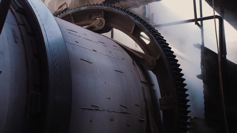 Rotating gear of huge industrial machine, steam on the background. Rotary kiln on a cement plant. Industrial production process of cement clinker or expanded clay. Huge industrial oven on a factory.
