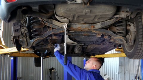Mechanic, examining the suspension of a vehicle with a steel rod for any undesired clearances as part of a periodical vehicle safety inspection or mot test