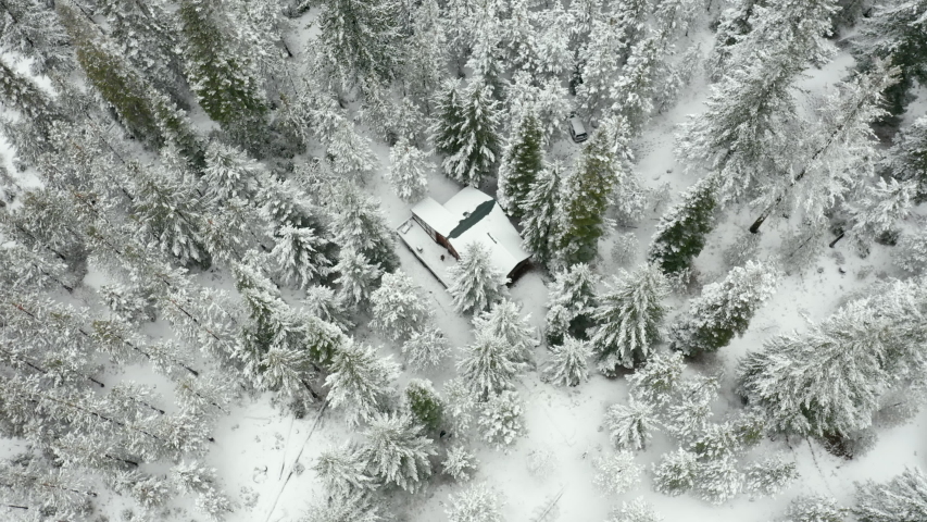 4k Aerial Long Video Circling Around a Cabin Surrounded by Snowy Trees