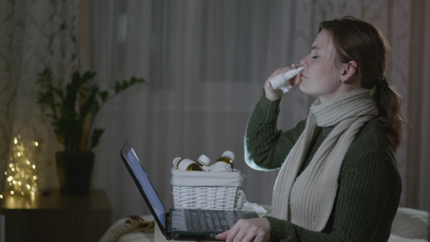 unhealthy woman coughs and uses medication for common cold, sneezes and suffers sore throat during flu and cold season, influenza adult girl is sitting at home on sick man with laptop lookin