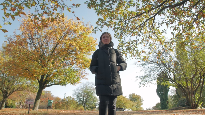 Girl walks autumn park yellow foliage serious young woman positive tracking camera movement