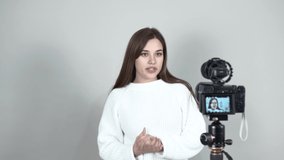 Light gray background Caucasian girl blogger white jumper Straight long hair stands in front of the camera, talking intently. Gestures the camera Screen is turned to the audience.