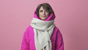 Beautiful young woman wearing winter jacket with a scarf smiling isolated over pink background