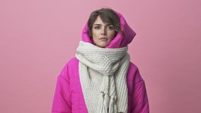 Nice young woman wearing a winter jacket with a scarf is sneezing isolated over a pink background