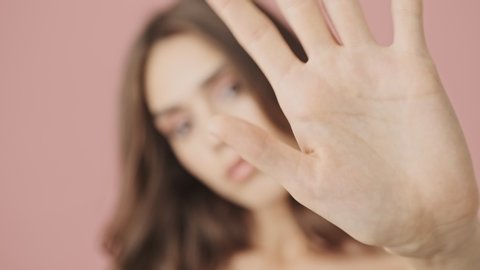 Close-up view of young half-naked woman is waving her hand in front of the camera isolated over pink background