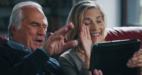 Close up of happy mature senior couple is making a selfie or video call with a tablet in living room at home.