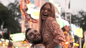 Happy smiling young man holding a beautiful woman in his arms in an amusement park