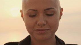 Close up view of Young attractive bald sports woman becoming happy and looking around near the sea outdoors