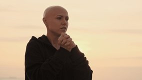 Concentrated attractive bald sports woman warming up her hands and looking away near the sea outdoors