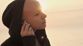 Side view of calm attractive bald sports woman using earphones and looking away while standing near the sea outdoors