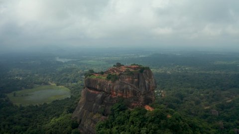 aerial view of the holy mountain Sigiriya. Circling around the mountain through the clouds. Mountain among palm trees and rice fields