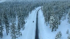 Drone footage over snow covered snowy pine trees with snow covered mountains and roads, winter wonderland, film video 