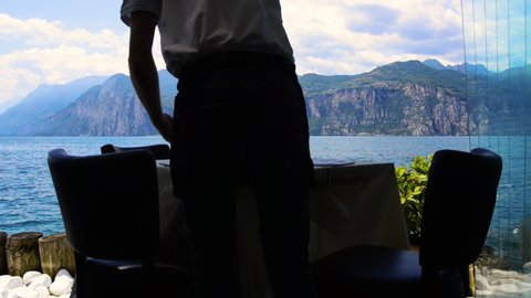 View of Lake Garda (Lago di Garda) from an Italian restaurant. Waiter cleaning and preparing a table in a restaurant