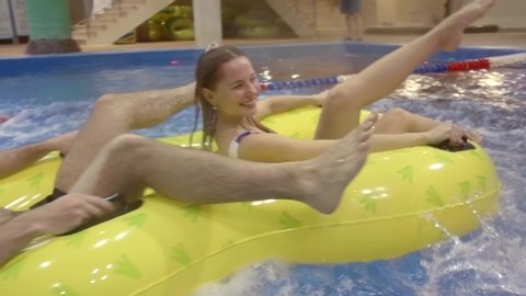 view from the bottom of the water on a green water slide. guy and girl ride out of it on a double inflatable yellow mattress