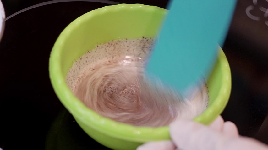 Someone is stirring milk mixed with chocolate with big blue knife, mix of milk and chocolate is put in green bowl and placed on blak oven in kitchen..