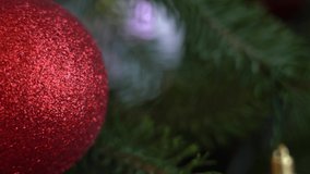 Closeup view of red Christmas (Xmas) shiny ball hanging on green branch of holiday xmas tree. Real time 4k video footage.