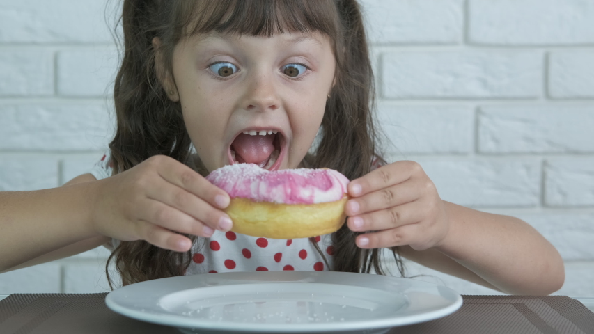 Sweet tooth day. Happy kid with big eyes eat a doughnut with glase.