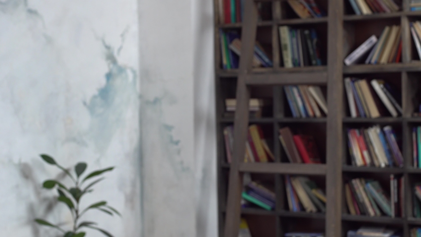 Young man standing in library holding pile of books looking camera unhappy