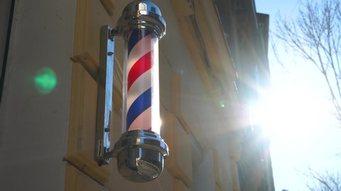 ashioned barber pole turning against orange building in a reflection of yesteryear. Barber shop pole. Logo of the barbershop, symbol. Barbershop pole, retro. Copy space. Old fashioned vintage barber