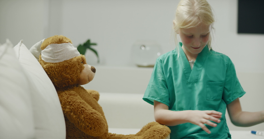 Cute little girl wearing doctor suit playing at home, performing a medical check-up her teddy bear. Shot on RED Cinema camera with Cooke Prime lenses