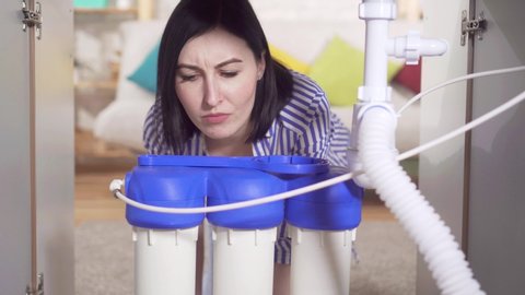 young woman housewife looks under the sink and examines the water filter
