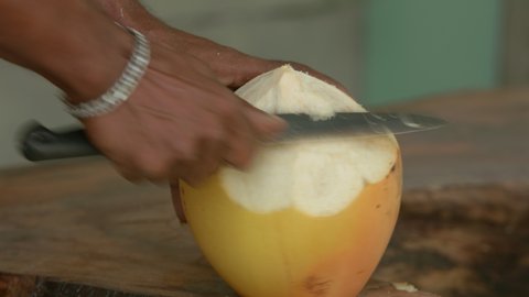 Close up of man peeling, shelling , cutting a yellow fresh coconut with a big knife for coconut juice. Hard work, manual labor and life without technology in tropical island concept. Maldives.