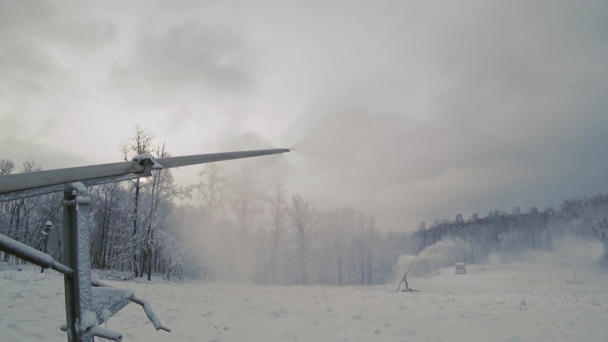 Close up of a snow making machine on a ski slope at a cloudy day. Snow fog flies in the air.