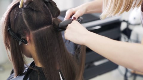 Close up, hairdresser styling long woman hair with hair iron in beauty salon. Process of hairstyling in barber shop