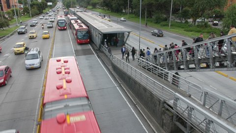 Bogotá, Colombia - December 16, 2019: View of Transmilenio bus public transport system with commuter people walking and highway traffic in Bogota, Colombia