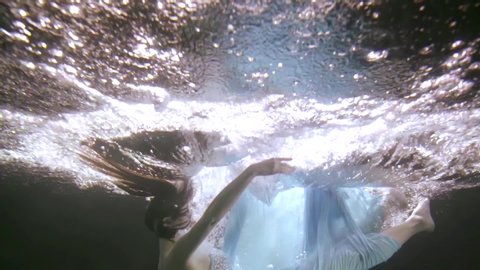 close up of a dark haired girl falling into the water she is underwater on a blue background. Splashes and splashes of water everywhere.
