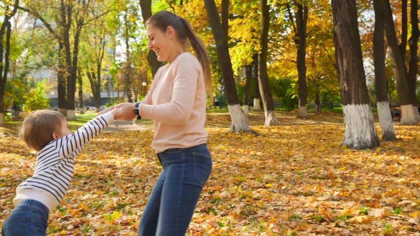 4k footage of happy young mother holding her little son by hands and rotating him in autumn park