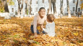 4k video of happy laughing little boy having fight with his mother with fallen leaves in autumn park