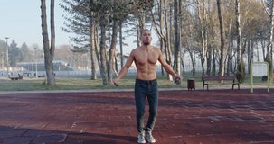 Male fitness model jumping rope in public park 
